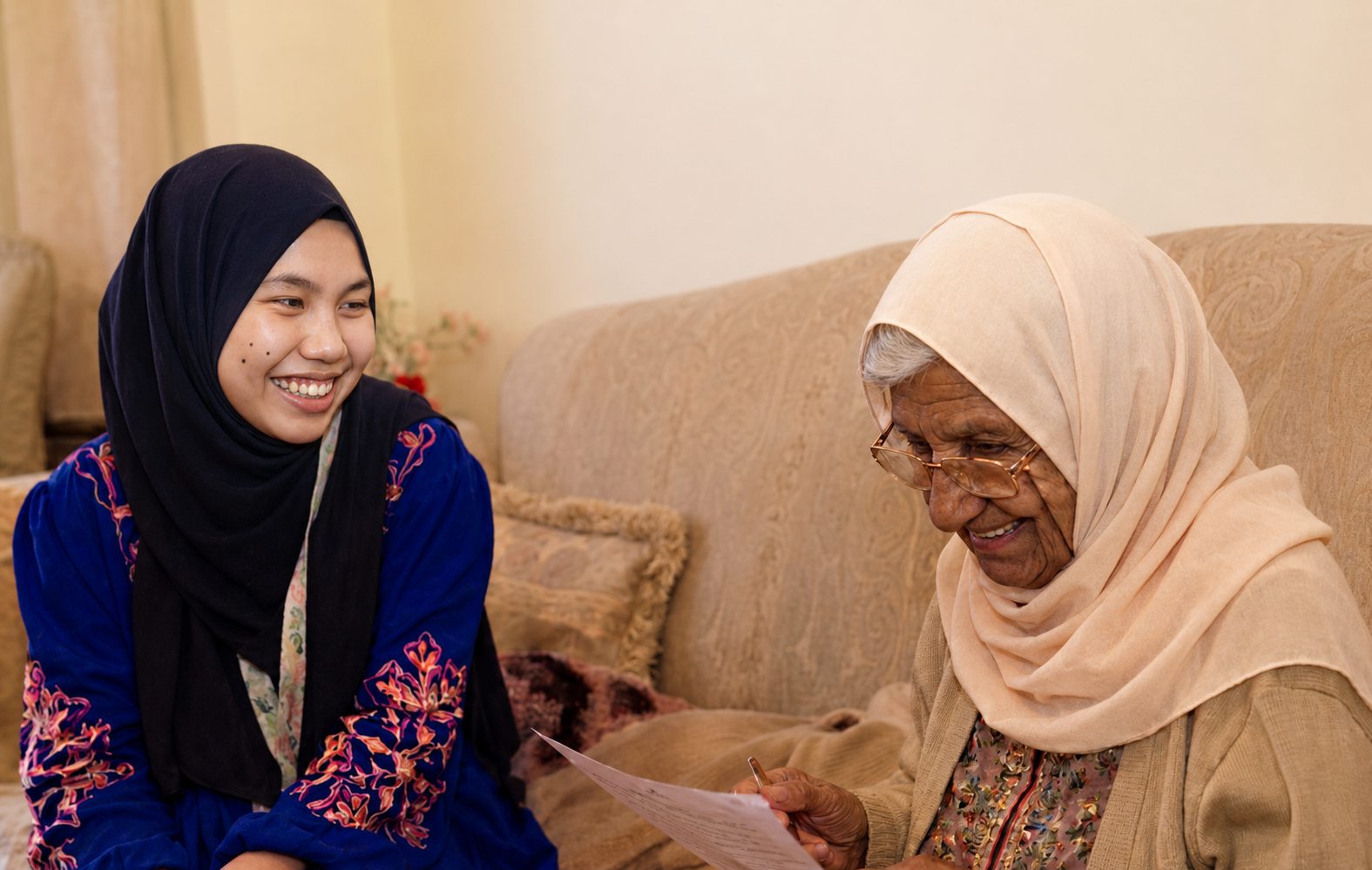 A carer sitting and laughing with an older woman in her living room.